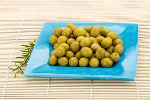 Green olives in a bowl on wooden background photo