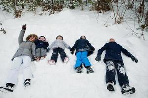 madre con cuatro hijos en la naturaleza invernal tumbados en la nieve. foto