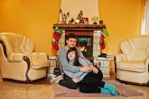 Happy young couple at home by a fireplace in warm living room on winter day. photo