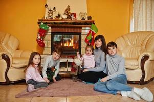 Happy young large family by a fireplace in warm living room on winter day. Mother with four kids at home. photo