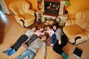 Happy young large family by a fireplace in warm living room on winter day. Mother with four kids at home. photo