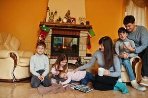 Happy young large family at home by a fireplace in warm living room on winter day. photo