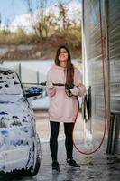 Brunette from a high-pressure hose applies a cleaner on the car photo