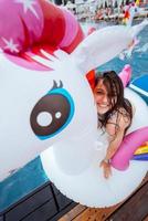 Happy young woman sitting on inflatable unicorn toy mattress photo