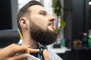 Barber works with a beard clipper. Hipster client getting haircut. photo