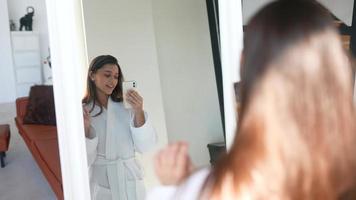 Young woman in robe video chats on smart phone standing before a mirror