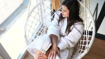 Young woman sits in macrame chair by window video