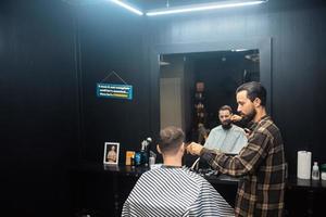 maestro en barbería hace corte de pelo de hombres con cortapelos foto