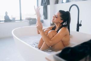 Young woman hugs her legs while sitting in the bath photo