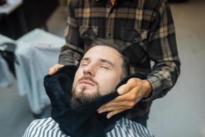 Barber preparing man face for shaving with hot towel in barber shop photo