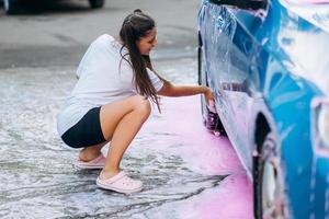 morena con dos coletas con una esponja lava el costado del auto foto