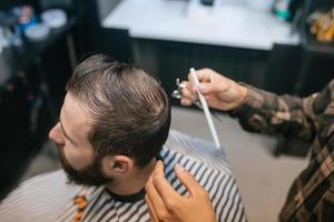 Cheerful young bearded man getting haircut by hairdresser at barbershop photo