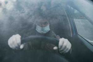 mujer joven con una máscara y guantes conduciendo un automóvil.