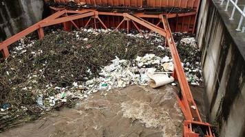 antenne visie van troebel bruin Woud water vrijgelaten door beton dam afvoer kanalen net zo water overstroomt in de regenachtig seizoen met droog twijgen en plastic verspilling Bij een dam poort in landelijk noordelijk Thailand. video