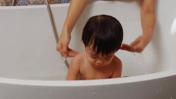 boy having fun bathing in the bathtub There is a mother sitting next to video