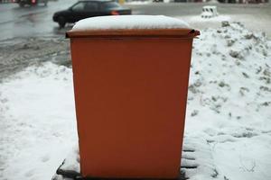 tanque de acero basurero lugar para almacenar arena en la carretera. objeto naranja en invierno en la carretera. foto