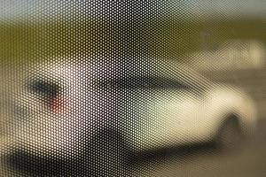 Mesh structure on glass of bus. Surface details of small holes. Blurry background shot through small holes. photo