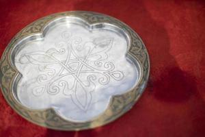 Steel dish with pattern. Plate on red cloth. Magician's inventory. photo