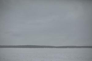 lago en invierno. día gris. clima nublado. campo nevado y bosque en el horizonte. foto