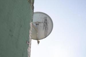 Old satellite dish on house. Dirt on antenna disc. Note TV signal.