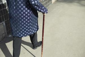 Grandma with walking stick. Woman walks on asphalt. photo