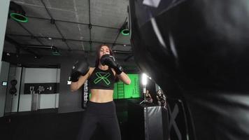 Woman in boxing gym kicks large bag with trainer video