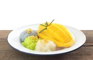 Famoso postre tailandés - plato de mango dulce fresco y maduro con arroz pegajoso blanco, verde y morado sobre una mesa de madera con fondo blanco foto