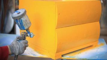 gelbe Bienenstöcke für Imkerei. Arbeiten Sie an der Lackierung eines Holzprodukts. Sprühfarbe auf die Möbeloberfläche. Bau eines Insektenhauses in der Werkstatt. Luftdruck drückt Ölfarbe heraus. video