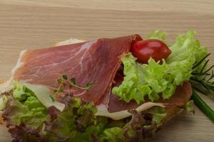 Prosciutto sandwich on wooden board and wooden background photo