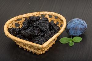 Dried plums in a basket on wooden background photo