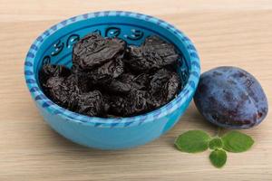 Dried plums in a bowl on wooden background photo