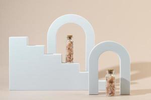 Two glass bottles with pink sea salt for spa procedures for face or body standing between geometric forms photo