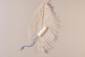 A woman personal hygiene cotton tampon lying on a light pink feather as a concept of freshness photo