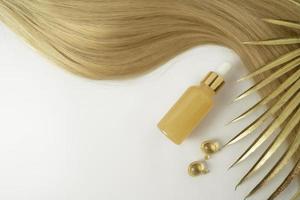 A beauty serum with vitamin C or smoothingoil for hair care lying near the strand of blonde hair photo