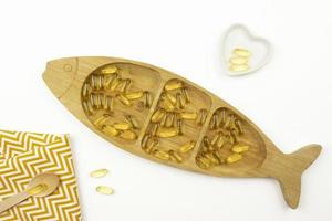 Yellow capsules of Omega 3 lie on a wooden plate in the form of the fish photo