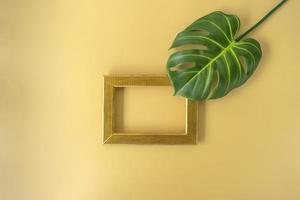 A golden frame with copy space and a green leave of monstera on it photo