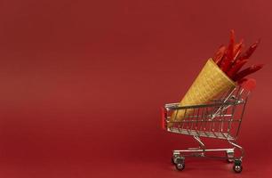 A waffle cone full of red hot chili peppers lies in a shopping trolley on a red background photo