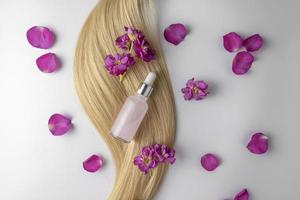 A pink face serum or oil made of rose petals with flower extract lying on a strand of blonde hair, product marketing mockup. A concept of hair care in a salon or at home photo