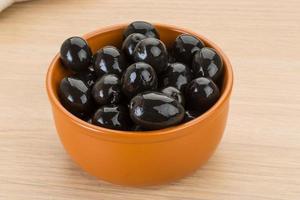 Black olives in a bowl on wooden background photo