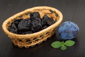 Dried plums in a basket on wooden background photo