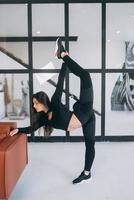 Young female wearing black sports suit stretching exercises indoors. photo