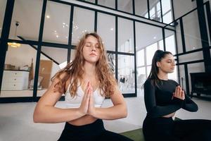 Two young women meditating in lotus pose with hands in namaste. photo