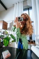 mujer joven alegre que hace la foto en la cámara en casa