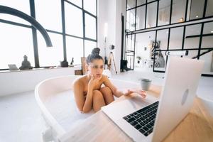 Young woman working on laptop while taking a bathtub photo