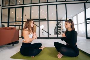 Two young women meditating in lotus pose with hands in namaste. photo