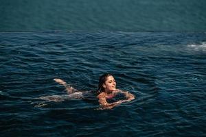 Happy woman in swimsuit swimming in infinity pool against seafront. photo