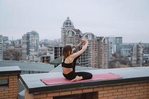 Woman practicing yoga on the mat on the roof and doing yoga exercises photo