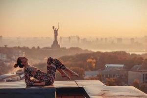 Woman doing yoga on the roof of a skyscraper in big city. photo