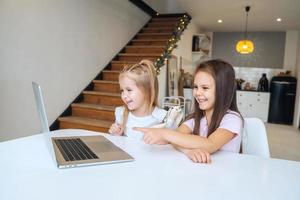 Two little girls playing together at the laptop while sitting at table photo