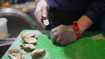 Hands of the cook opening an oyster. Close view photo